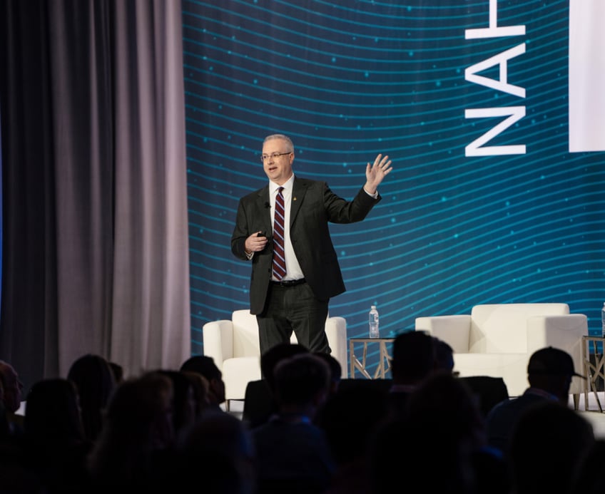 Man wearing a dark suit stands on stage